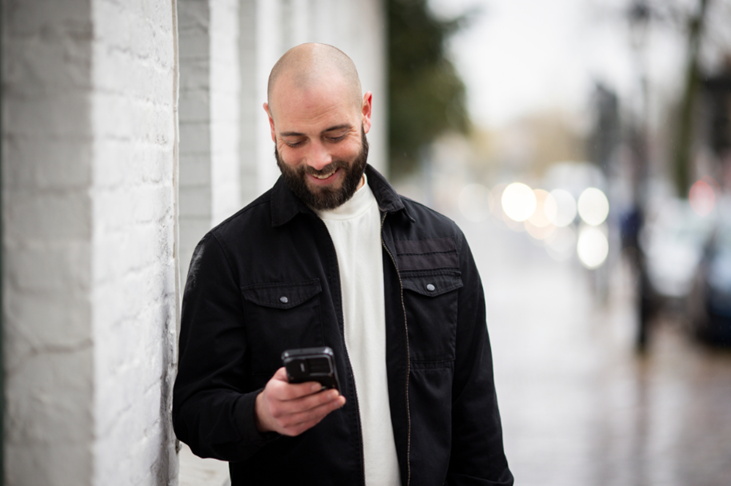 Beziehungscoach Florian Pohl steht entspannt im Freien und blickt auf sein Smartphone.