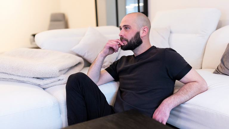 Mann sitzt nachdenklich auf einem Sofa – Symbolbild für die Frage: „Woran bemerke ich, dass mein Ex noch nicht über die Trennung hinweg ist?“